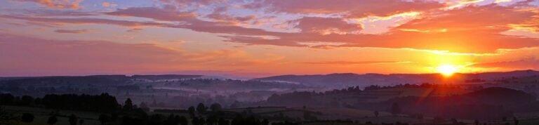 Stunning sunrise over rolling hills with colorful clouds and a vivid skyscape.